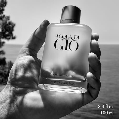Hand holding Acqua di Gio perfume bottle in grayscale.