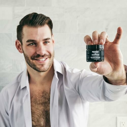 Man holding a skincare product jar in a bathroom.